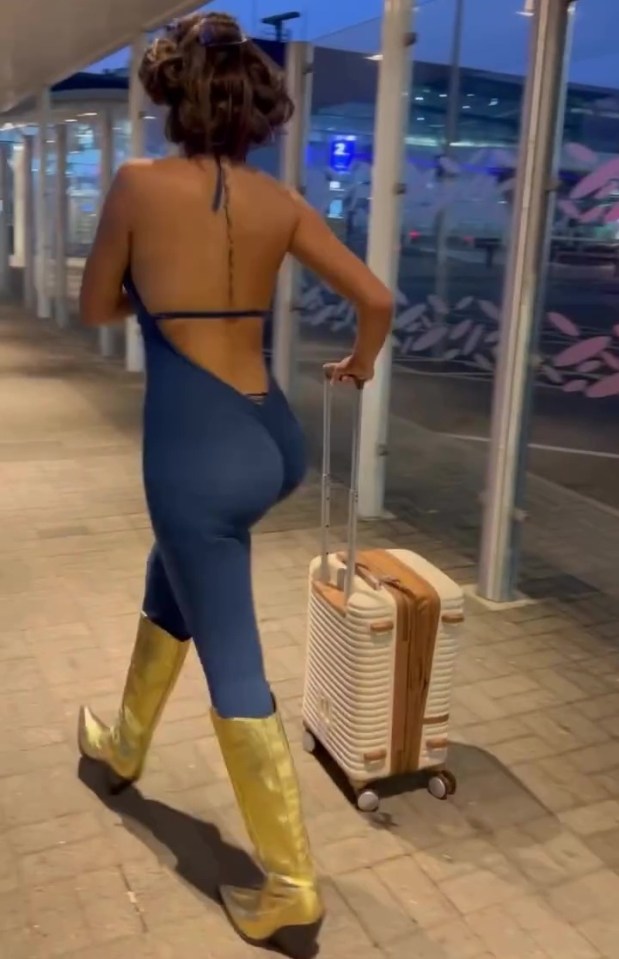 a woman in a blue jumpsuit and gold boots is pulling a suitcase