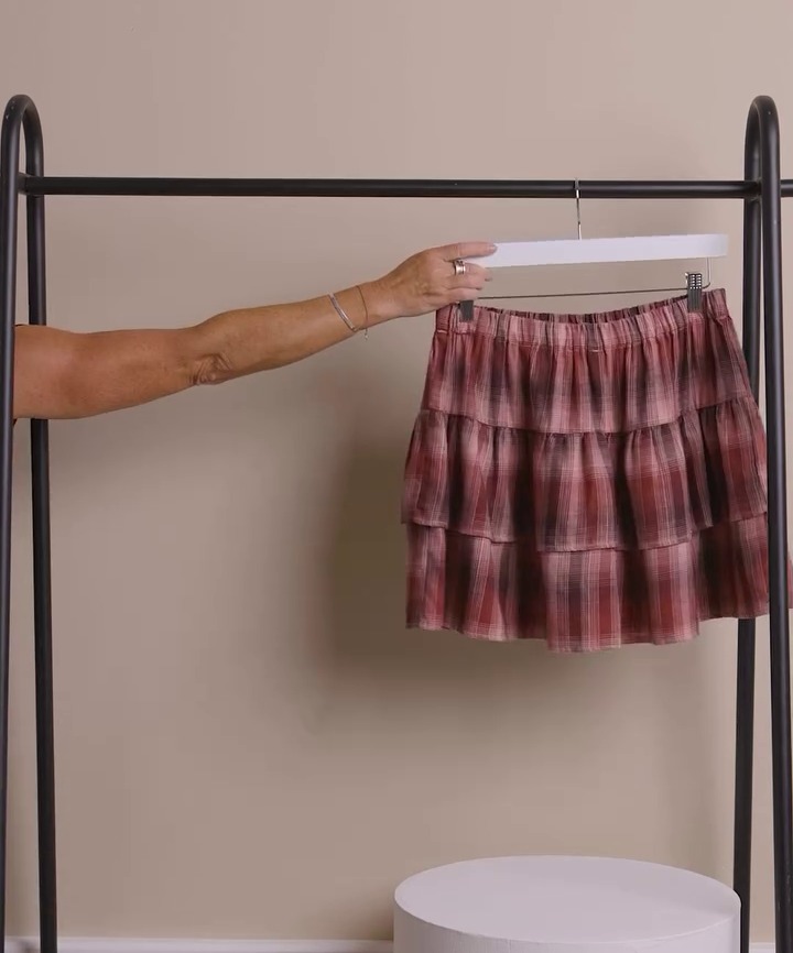 a woman is holding a plaid skirt on a rack