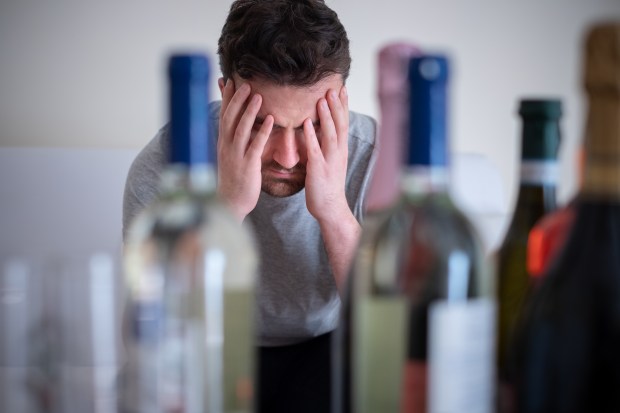 a man with his head in his hands looking at bottles of alcohol