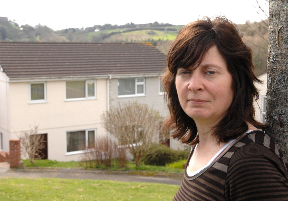 a woman leans against a tree in front of a house