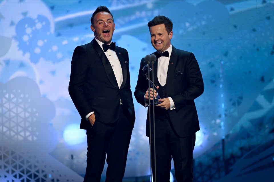 two men in tuxedos stand next to each other on a stage