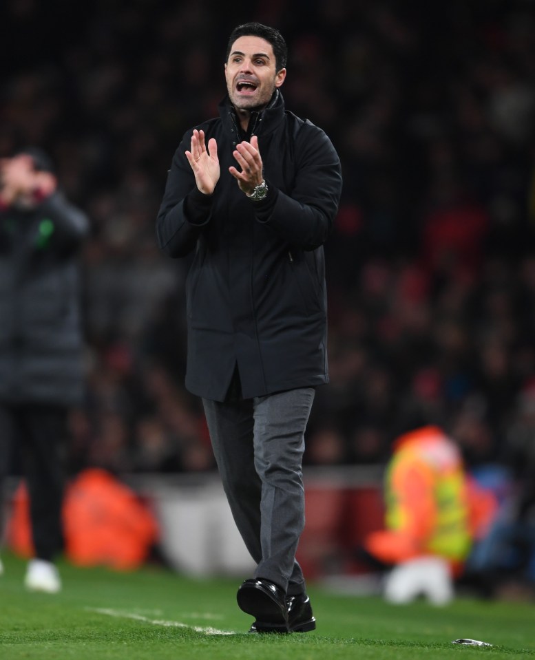 a man in a black jacket applauds on a soccer field