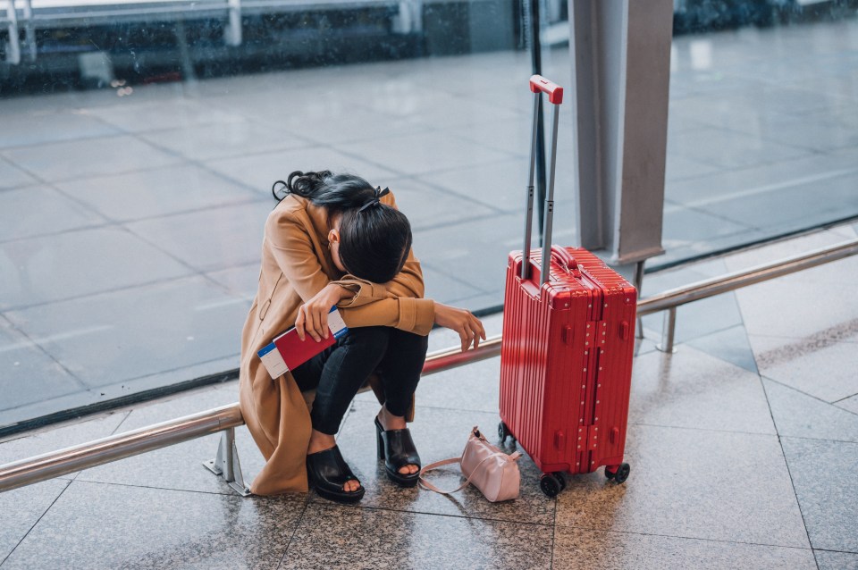 a woman sits on a bench next to a red suitcase