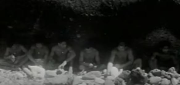 a group of men are sitting around a fire in the dark .