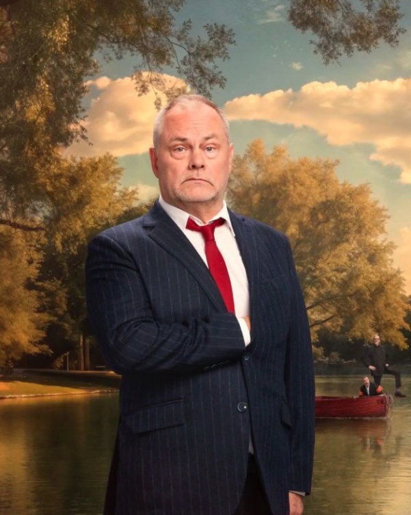 a man in a suit and tie stands in front of a lake