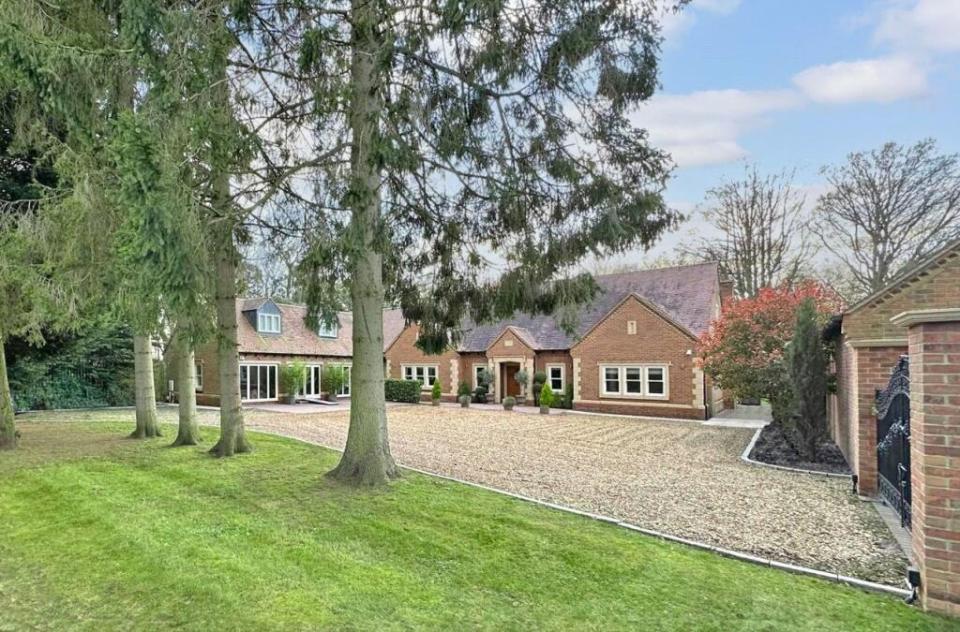 a large brick house with a gravel driveway surrounded by trees