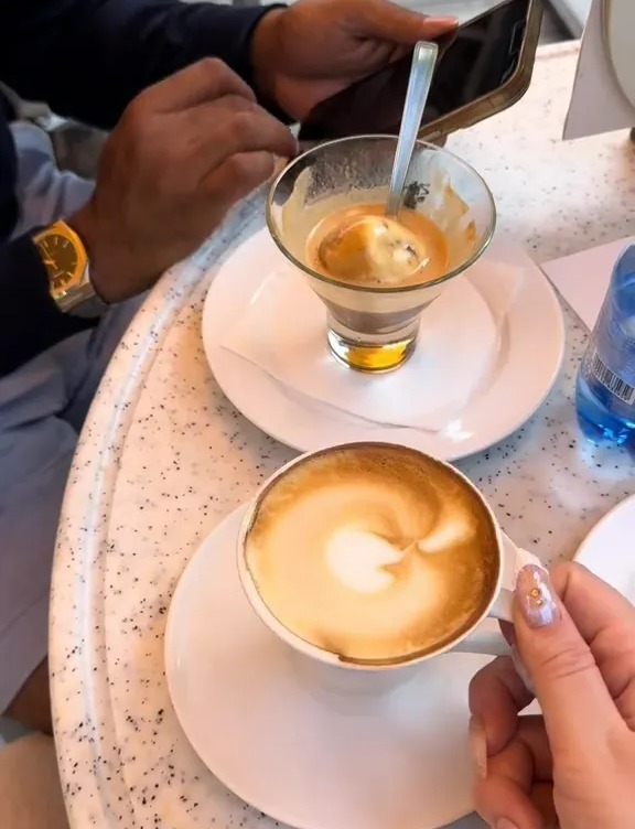 two cups of coffee on a table with a man looking at his phone