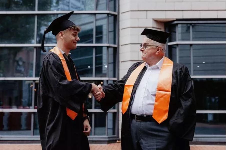 a man in a graduation cap and gown is shaking hands with a young man in a graduation cap and gown .