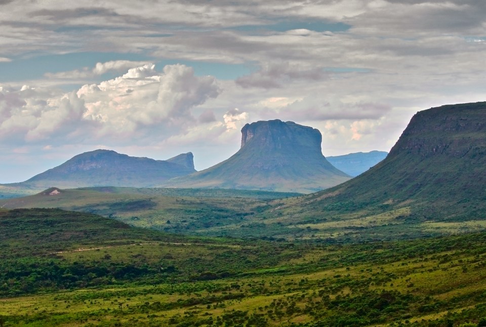 a valley with mountains in the background and a cloudy sky