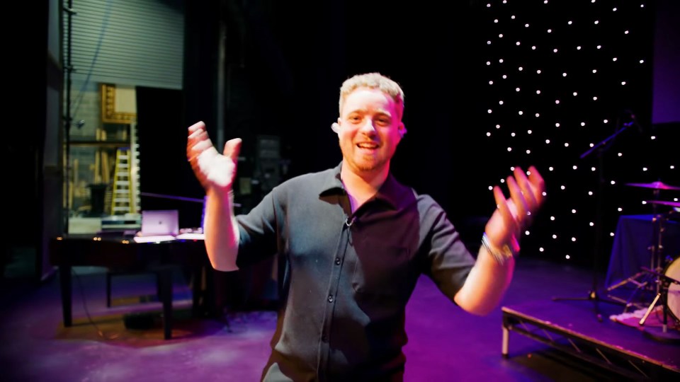 a man in a black shirt stands on a stage with his arms outstretched