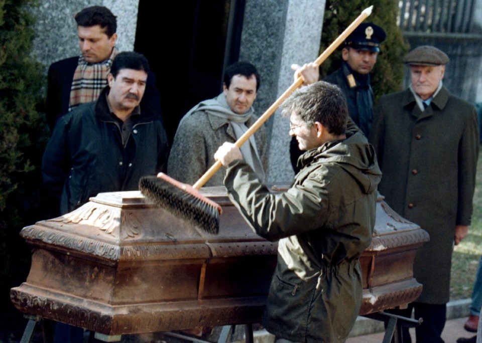 a man in a green jacket is cleaning a coffin with a broom