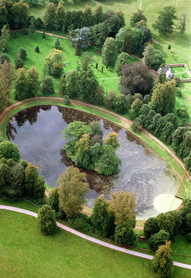 an aerial view of a pond surrounded by trees and grass