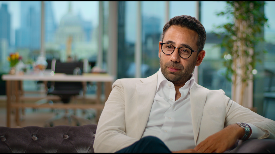 a man wearing glasses and a white jacket sits on a couch