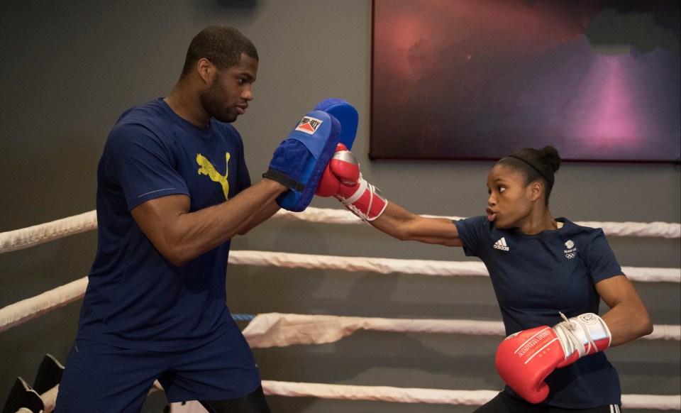 a woman wearing red boxing gloves is practicing with a man wearing a puma shirt