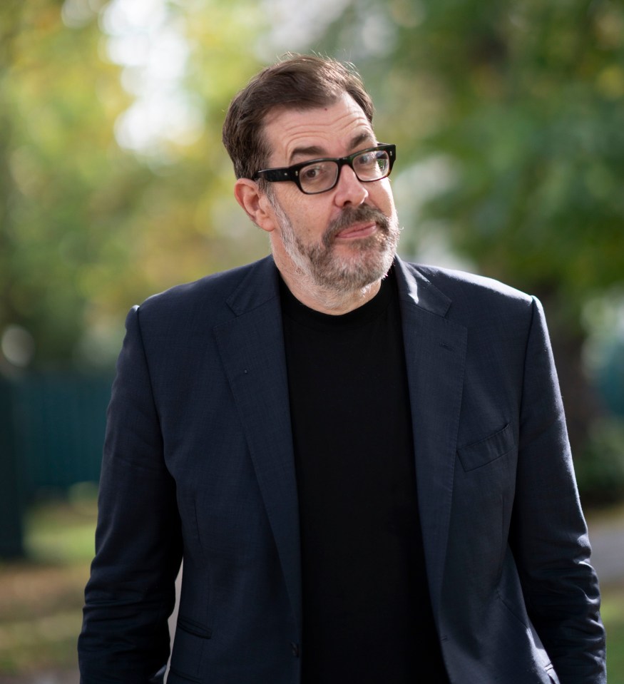 a man wearing glasses and a suit stands in front of trees