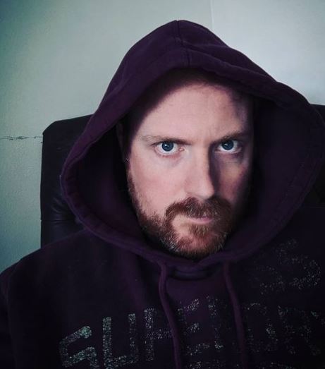 a man with a beard is wearing a purple hoodie and sitting in a chair .