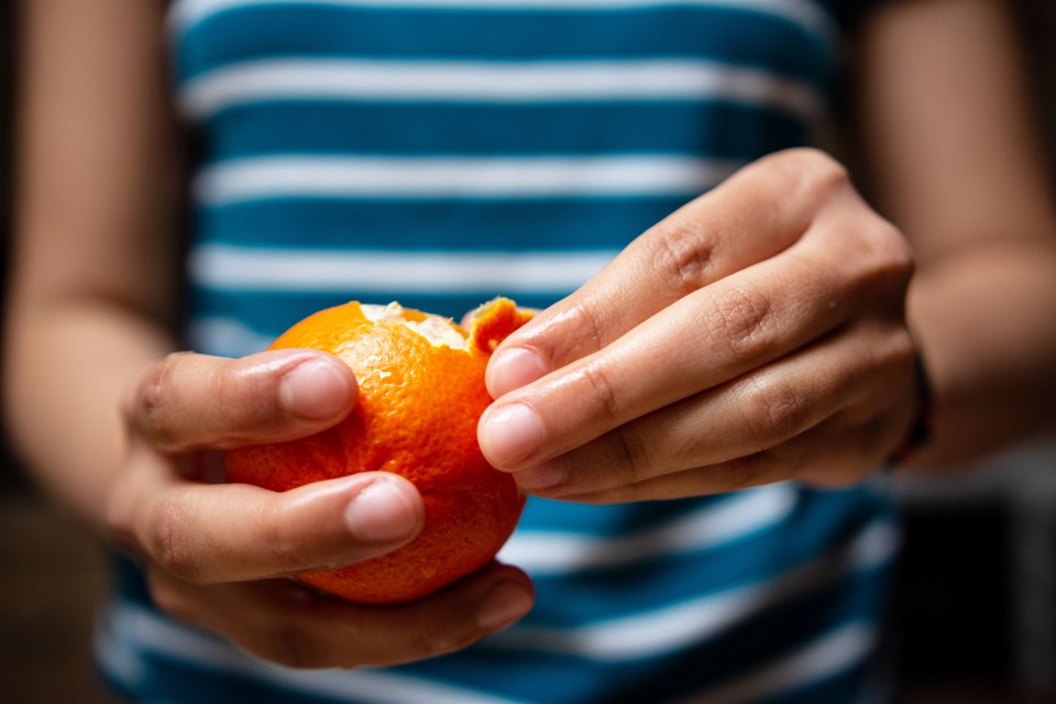 a person in a blue and white striped shirt is peeling an orange