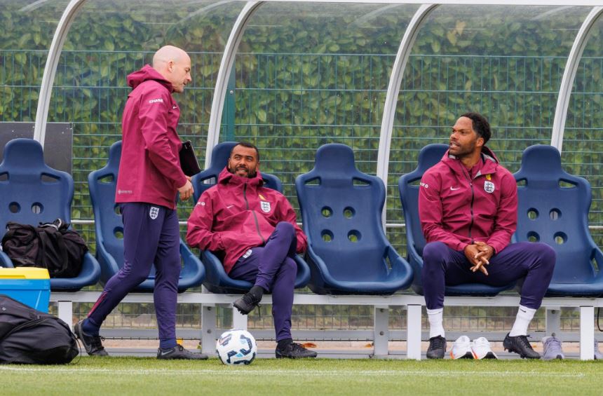 three soccer players sit on a bench with one wearing a jacket that says ' england ' on it