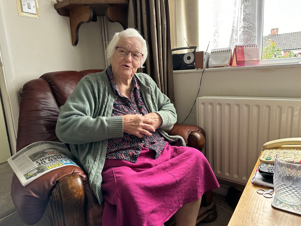 an elderly woman sits in a chair with a newspaper on her lap that says free trade