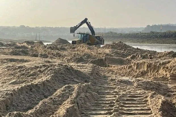 a large excavator is working on a pile of sand near a river .