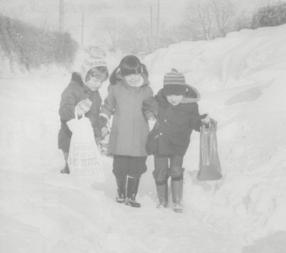 a black and white photo of children walking through the snow