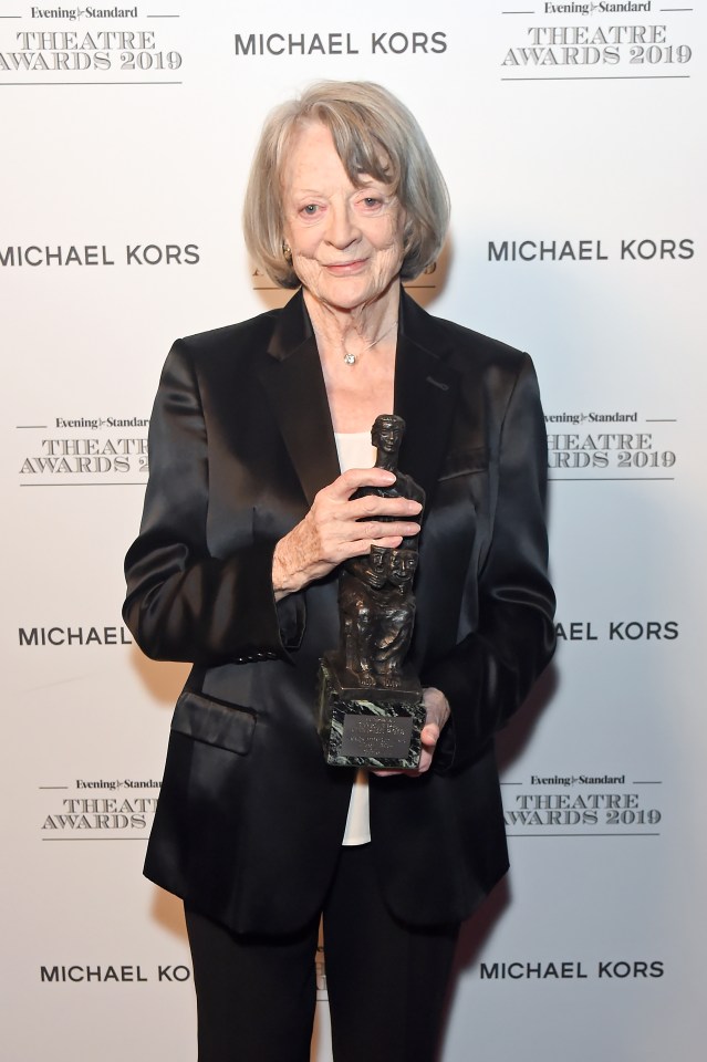 a woman holding a trophy in front of a michael kors sign