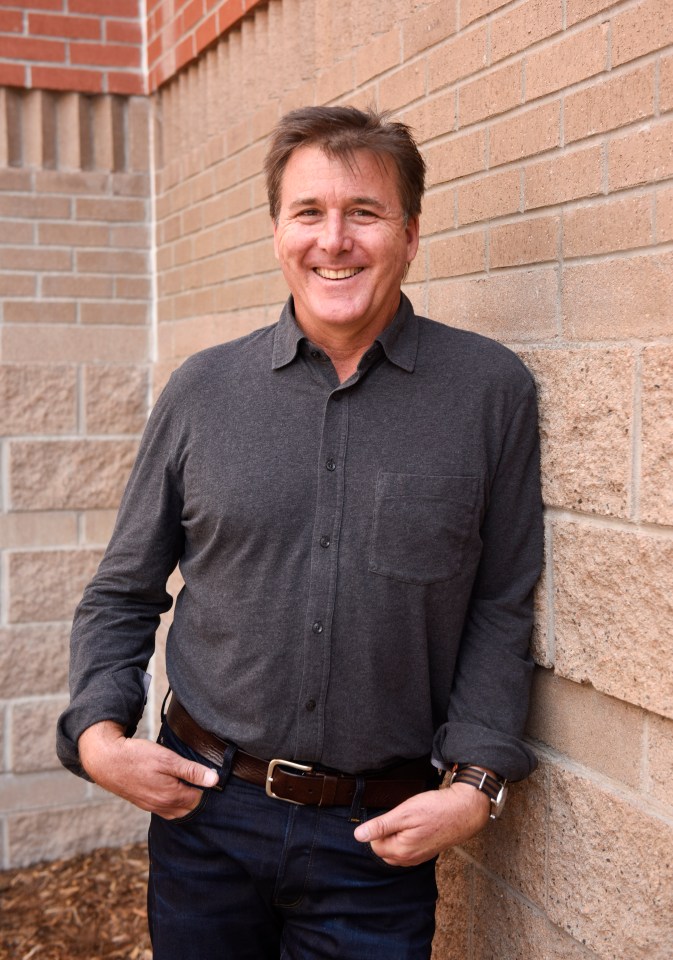 a man leaning against a brick wall with his hands in his pockets