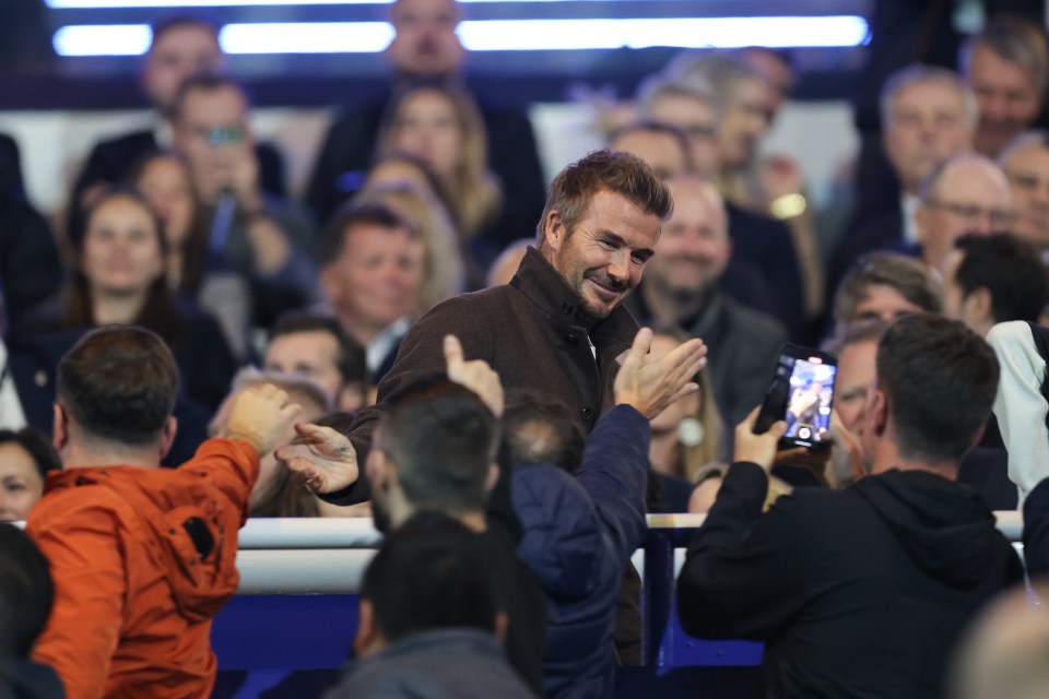 a man in a brown jacket stands in a crowd of people