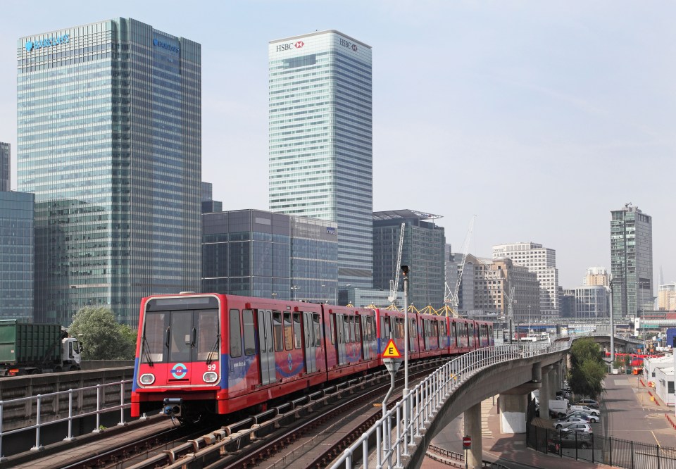 a red train is going down the tracks in front of a hsbc building