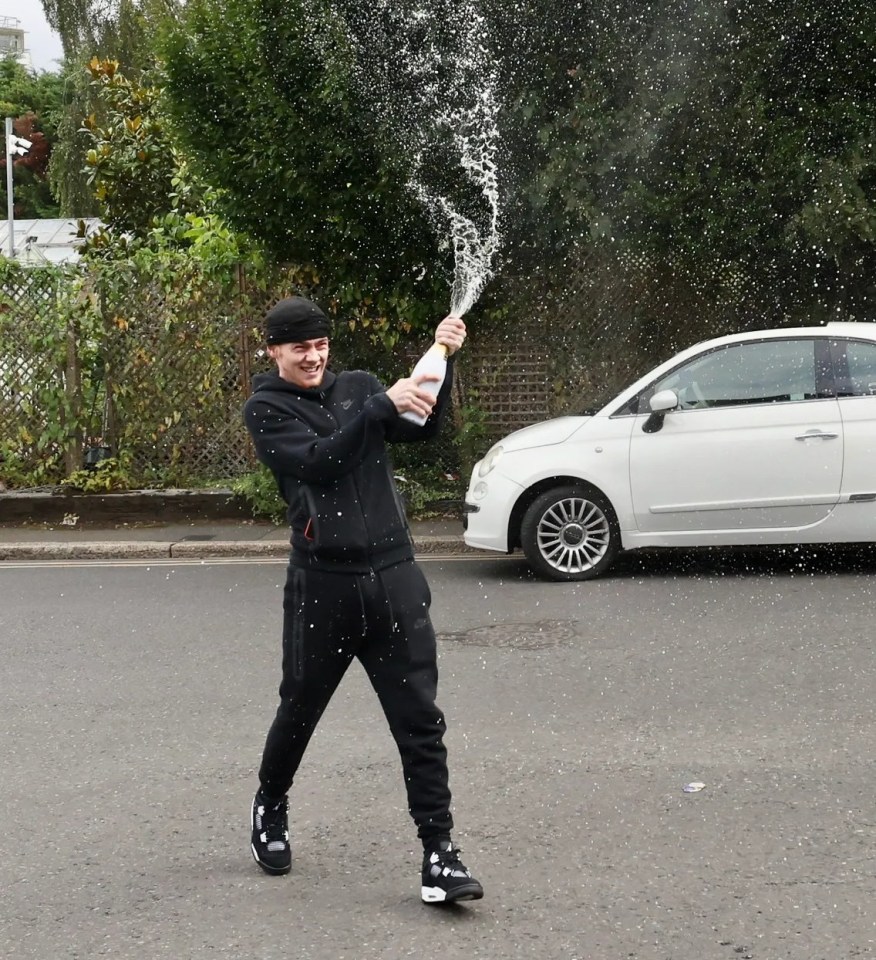 a man is holding a bottle of champagne in front of a white car