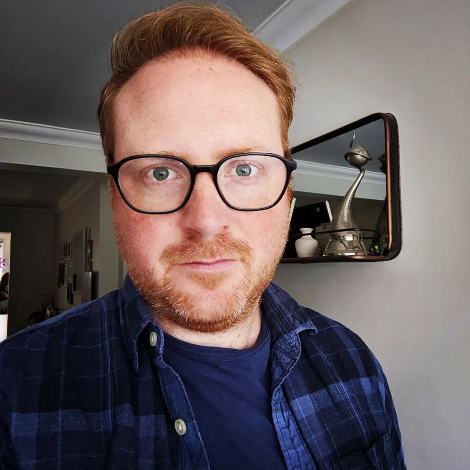 a man wearing glasses and a plaid shirt stands in front of a mirror