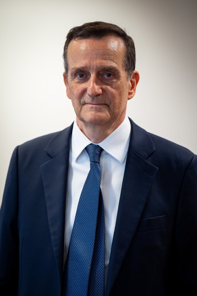 a man in a suit and tie stands in front of a white wall