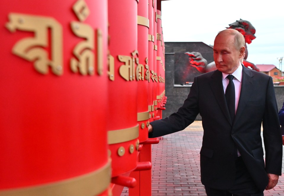 a man in a suit stands in front of a row of red cylinders with chinese writing on them