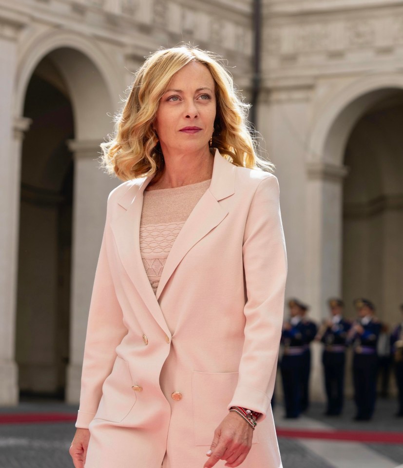 a woman in a pink suit stands in front of a building