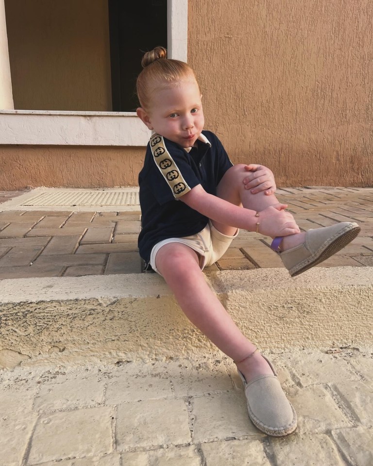 a little boy wearing a gucci shirt sits on the sidewalk