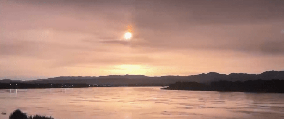 the sun is setting over a river with mountains in the background