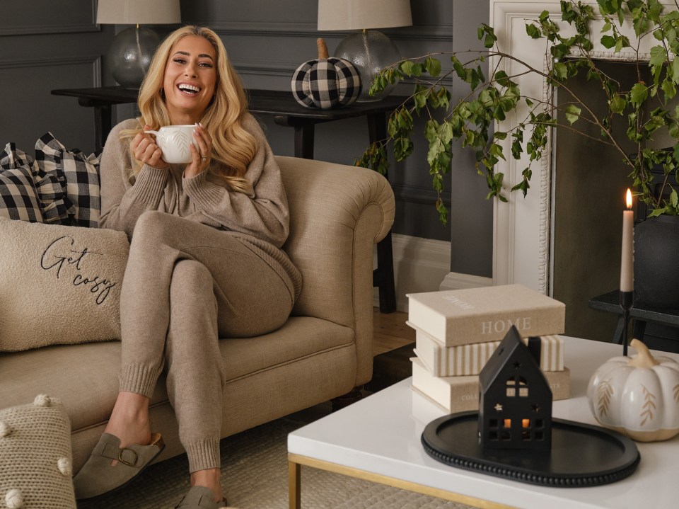 a woman sits on a couch with a pillow that says get cosy