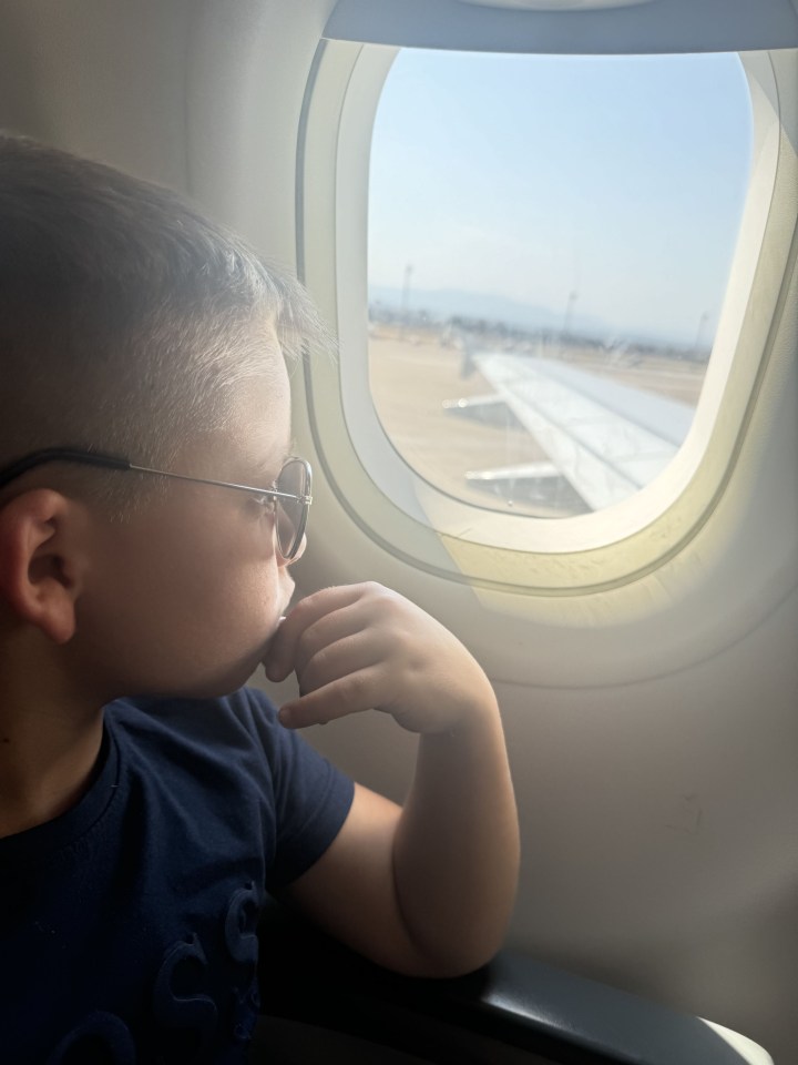 a young boy wearing glasses looks out the window of an airplane