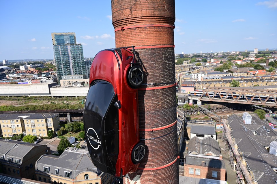 a red nissan car is attached to a brick chimney