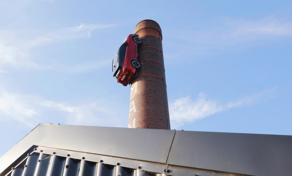 a red car is hanging from a brick chimney