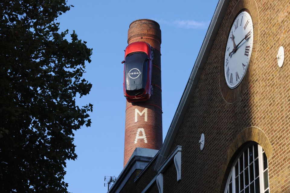 a red nissan car is hanging from a brick chimney