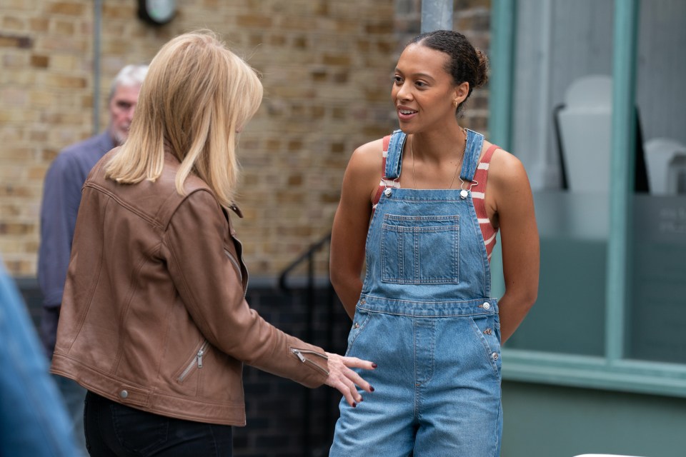 a woman in overalls is talking to another woman