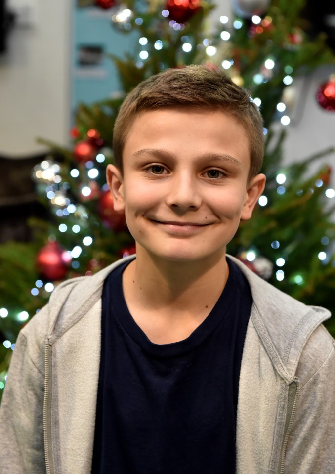 a young boy smiles in front of a christmas tree