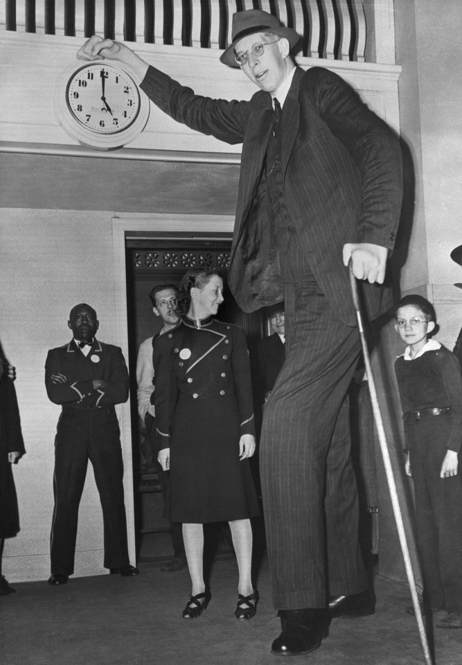 a man in a suit holds up a clock with the hands on the numbers 1 through 12