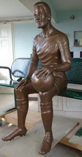 a bronze statue of a soccer player sitting on a bench