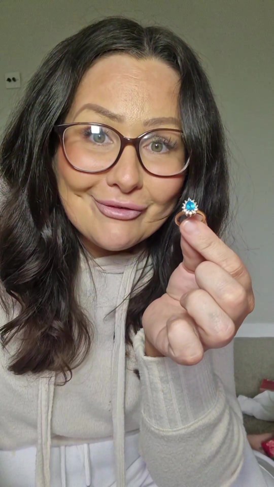 a woman wearing glasses is holding a small ring in her hand