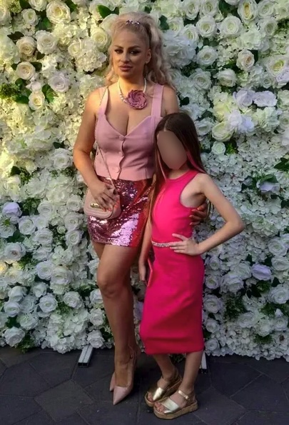 a woman and a little girl are posing for a picture in front of a wall of flowers .