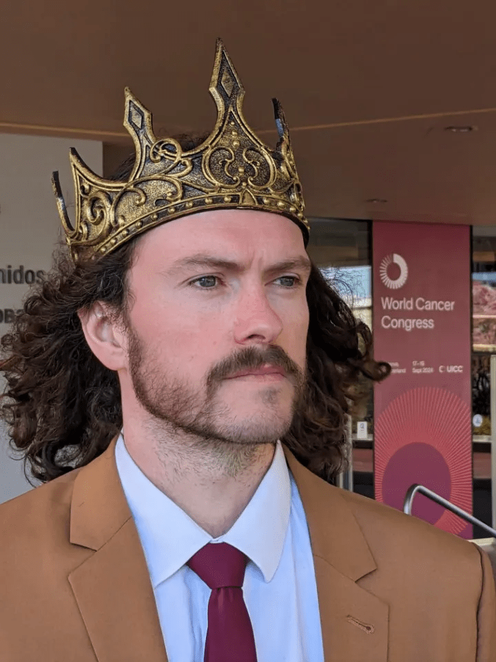 a man wearing a crown stands in front of a world cancer congress sign