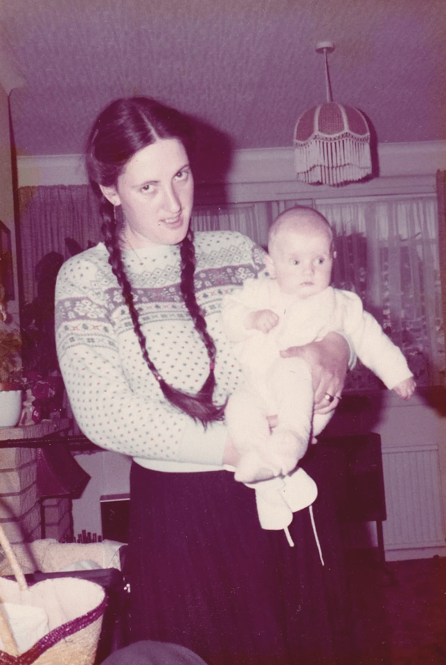 a woman in a sweater holds a baby in her arms