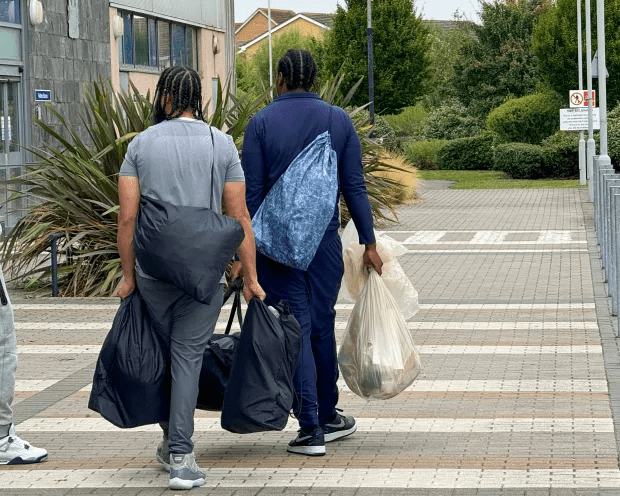 two people are walking down a sidewalk carrying bags